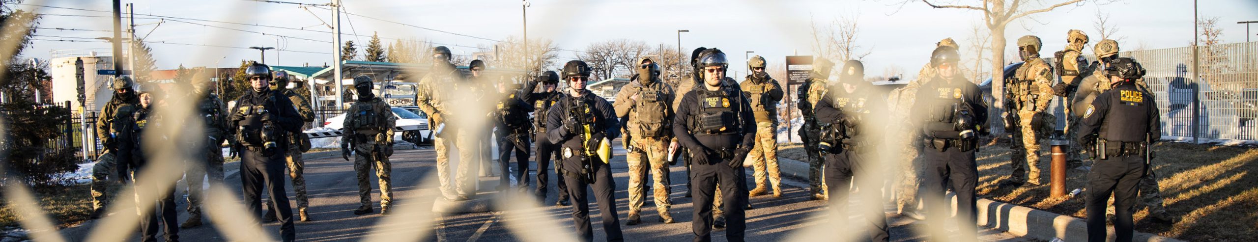 Federal enforcement officers stand behind a chain-link fence during Operation Metro Surge
